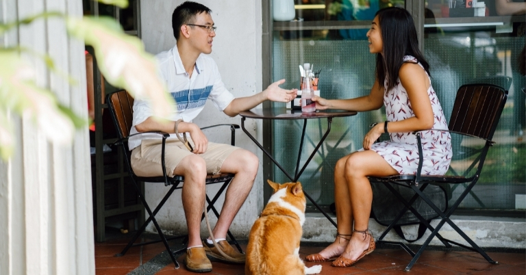 Couple sitting at an outdoor cafe with a dogg